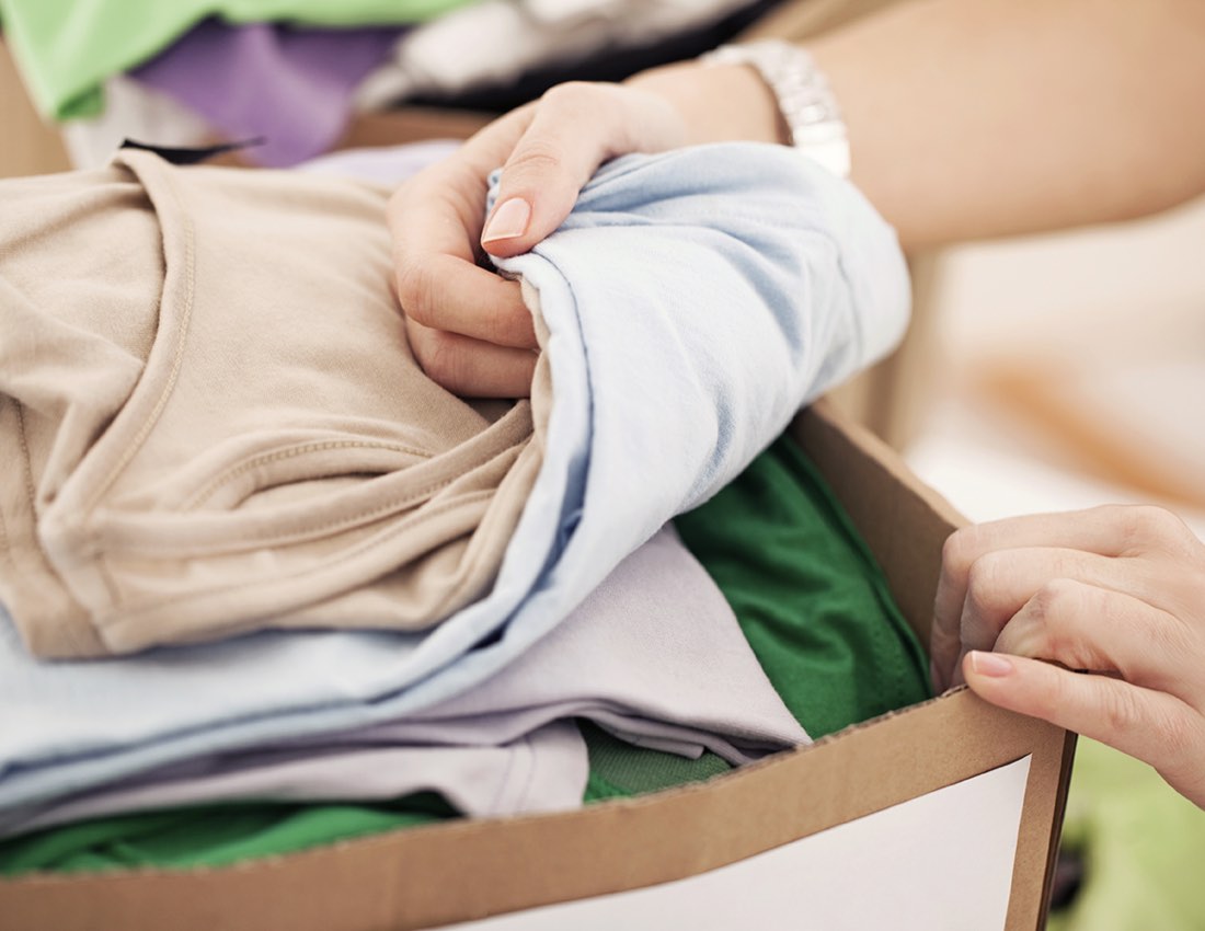 Hands folding donated clothing into a box