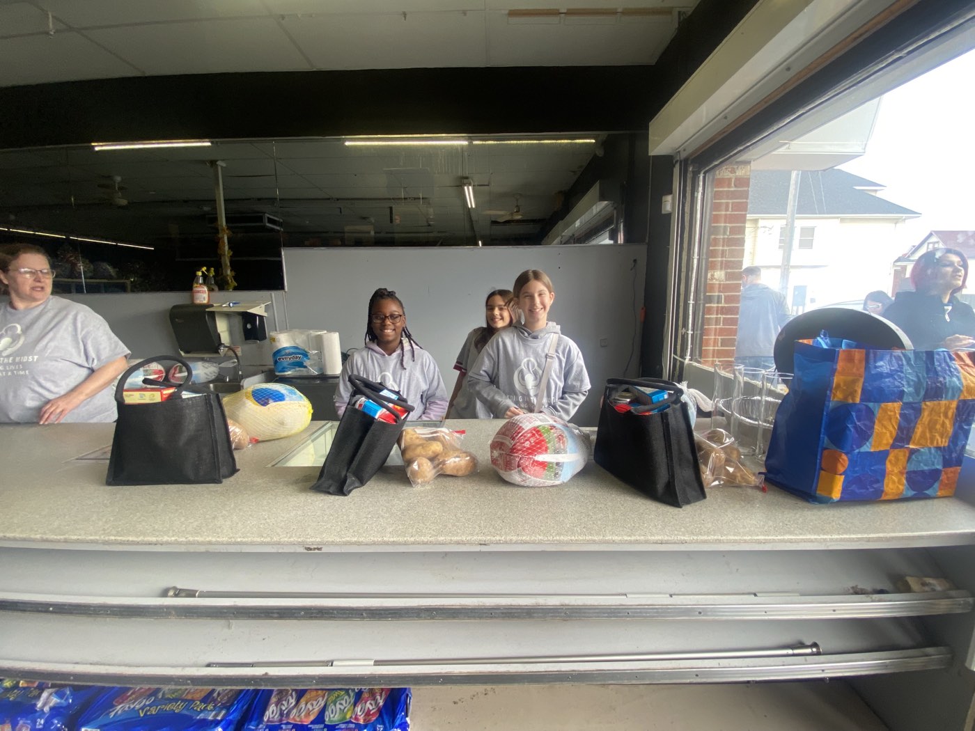 Volunteers behind a distribution counter stacked with packed food bags and groceries